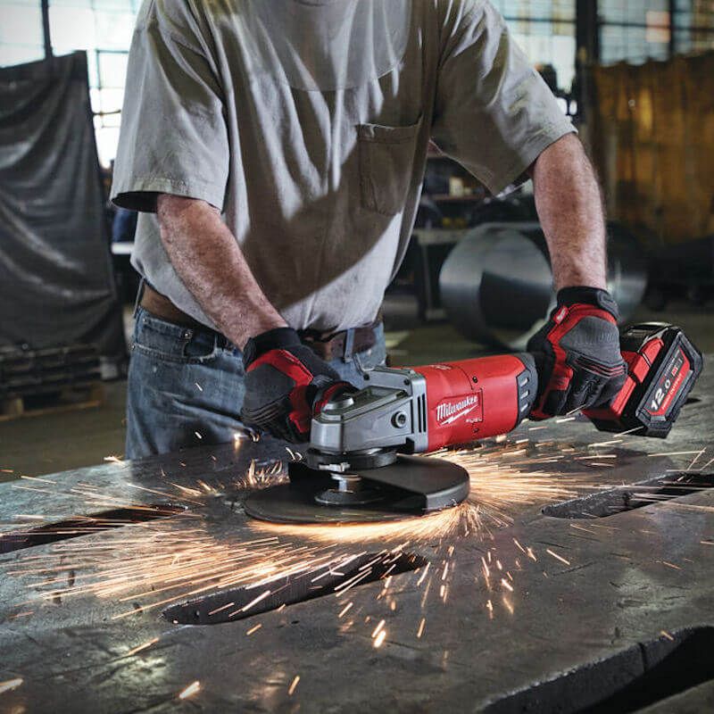 Milwaukee M18 FUEL 230mm Braking Grinder in use, cutting through stainless steel pipe with operator holding the anti-vibration side handle